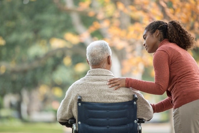 lady in red top placing caring hand of man with grey hair in wheelchair