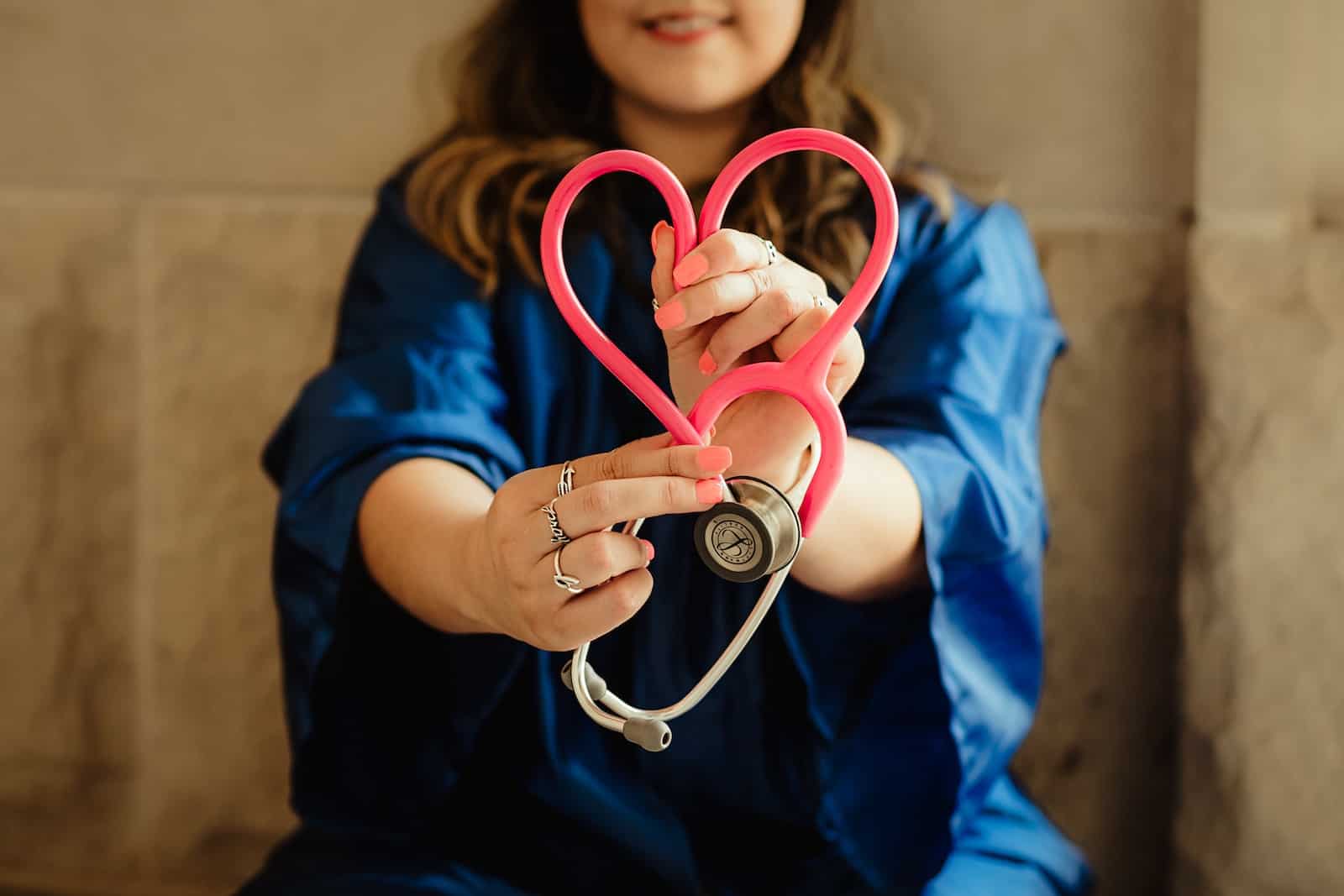 girl in blue scrubs holding pink and silver stethoscope in shape of a heart